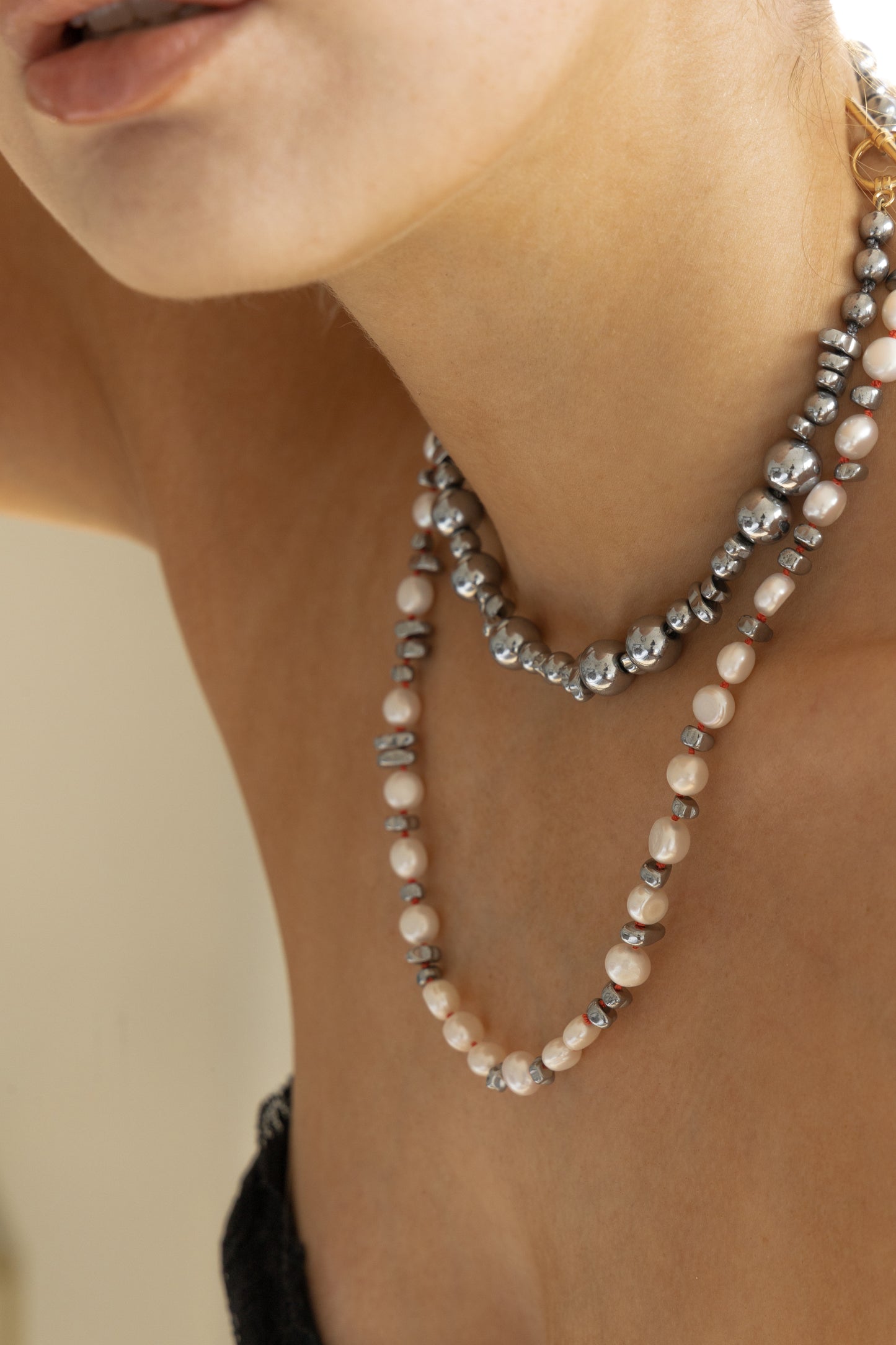 Female wearing a hematite beaded necklace layered with a pearl and hematite beaded necklace.