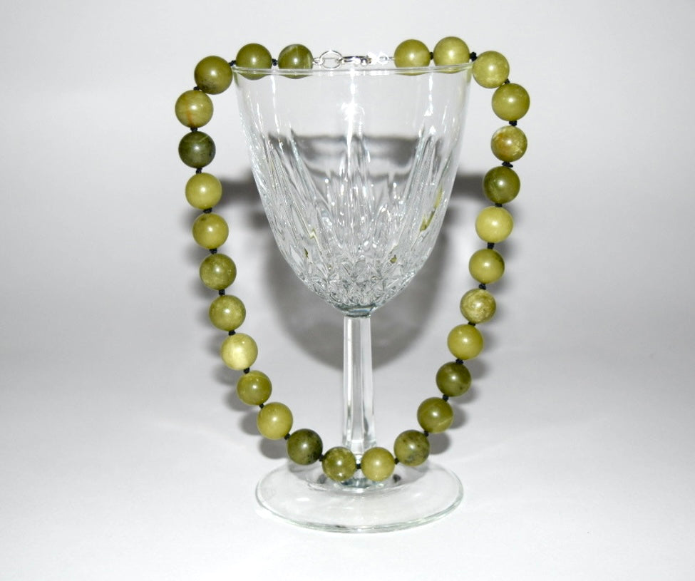 12mm chinese jade beaded necklace draped over a crystal wine glass on a white background.