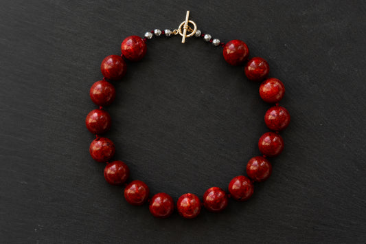 Red fossil coral beaded necklace with hematite beads and a gold toggle clasp on a black background