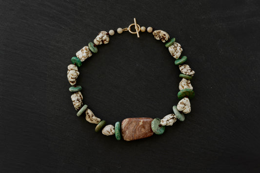 A magnesite, ancient maya jade, and jasper beaded necklace with a gold toggle clasp on a black background