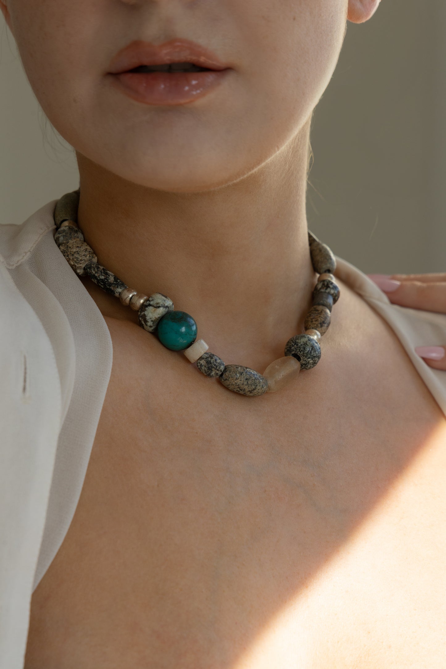 Close up of a female neck wearingan ancient mali granite, ancient mali quartz, ethiopian metal and turquoise beaded necklace